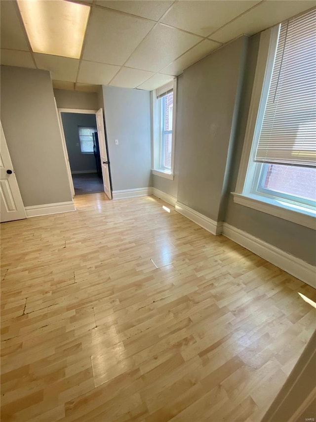 empty room featuring baseboards, a paneled ceiling, and light wood-style flooring