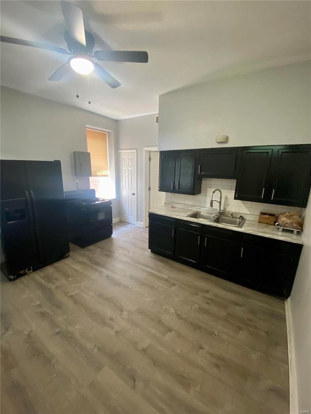 kitchen with a sink, black refrigerator with ice dispenser, dark cabinets, backsplash, and light wood-style flooring