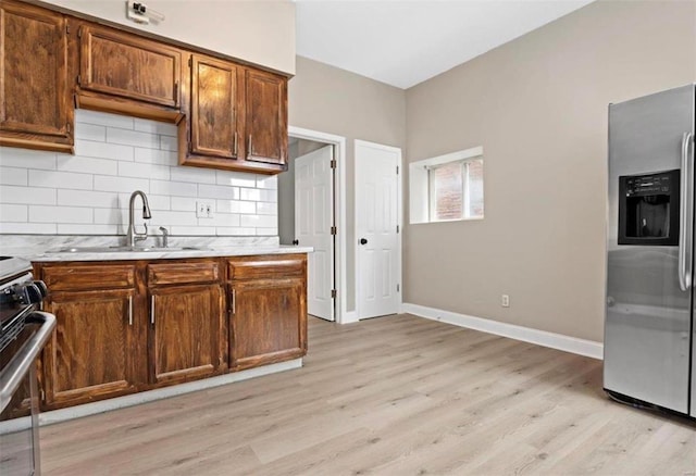 kitchen featuring stainless steel fridge with ice dispenser, a sink, light countertops, light wood finished floors, and decorative backsplash