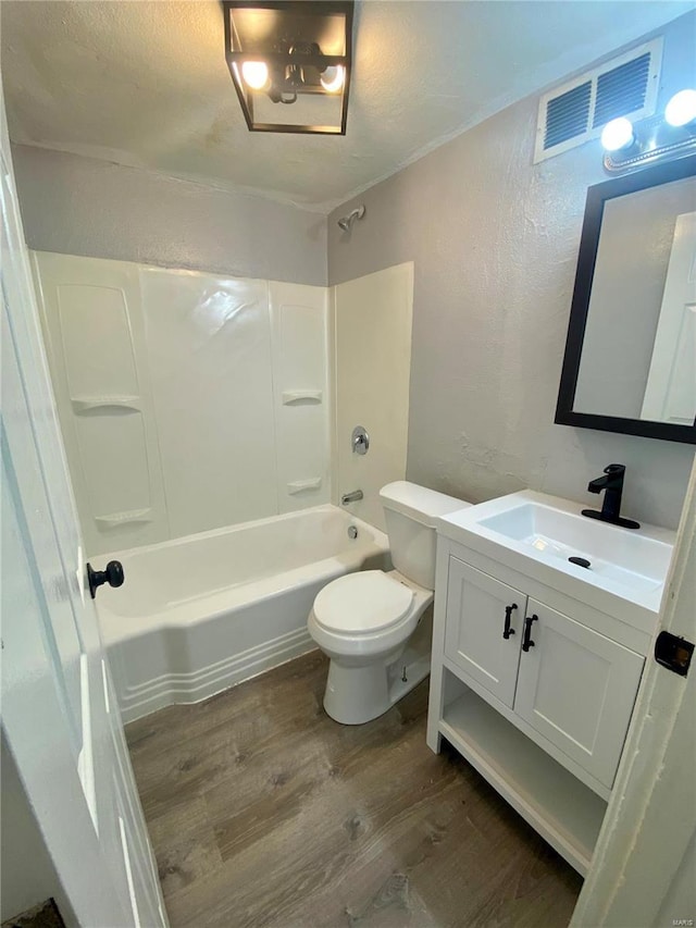 full bath featuring wood finished floors, a textured wall, shower / washtub combination, vanity, and toilet