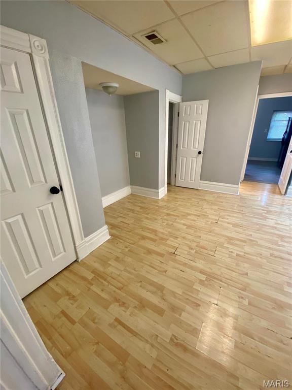 basement featuring a paneled ceiling, light wood-type flooring, and baseboards