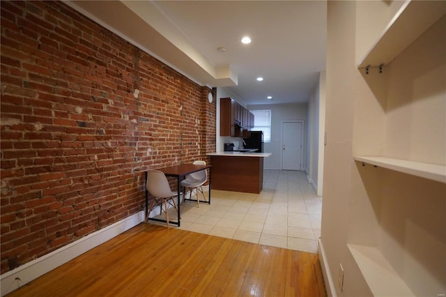 kitchen with baseboards, a peninsula, light wood-style flooring, brick wall, and light countertops
