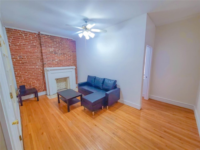 living area featuring light wood-style floors, a brick fireplace, a ceiling fan, and baseboards