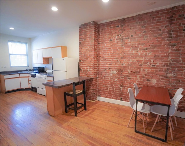 kitchen with white appliances, dark countertops, light wood finished floors, brick wall, and white cabinetry