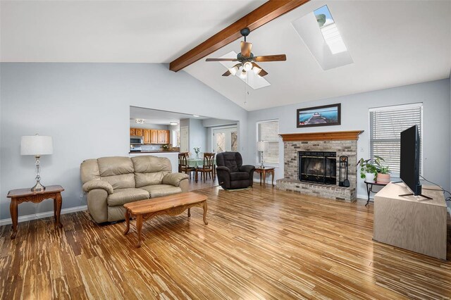 living room featuring light wood-style flooring, a ceiling fan, a brick fireplace, a skylight, and baseboards