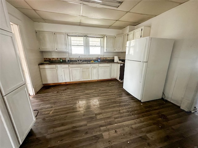kitchen with freestanding refrigerator, a drop ceiling, a sink, dark countertops, and dark wood-style flooring