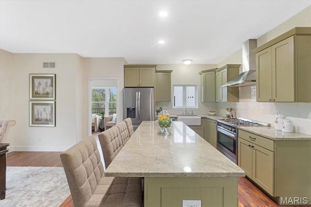 115 Place De Yeager, Lake St Louis, MO 63367 - kitchen featuring appliances with stainless steel finishes, wall chimney range hood, a breakfast bar area, a kitchen island, and backsplash