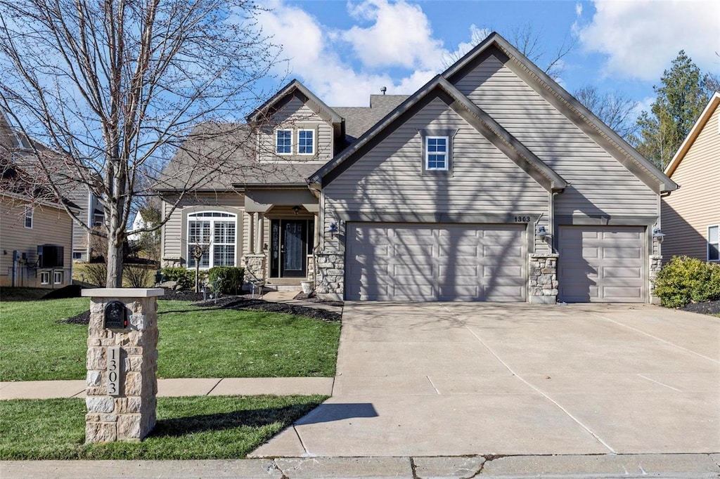 traditional home featuring driveway, a front yard, stone siding, and a garage