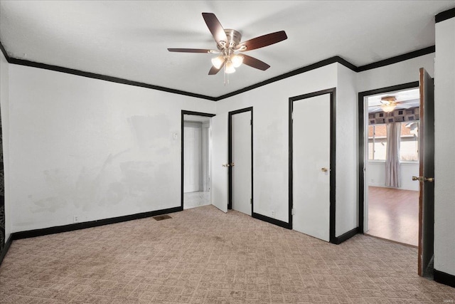 unfurnished bedroom featuring crown molding, carpet flooring, ceiling fan, baseboards, and multiple closets
