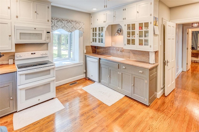 kitchen with white appliances, gray cabinets, light wood-style flooring, glass insert cabinets, and a sink