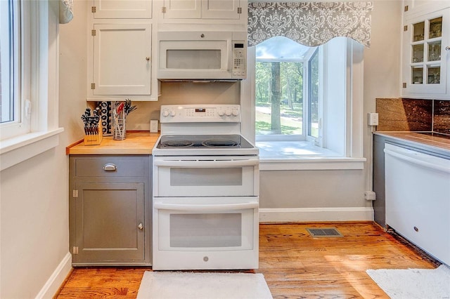 kitchen with white appliances, light wood-type flooring, gray cabinetry, glass insert cabinets, and baseboards