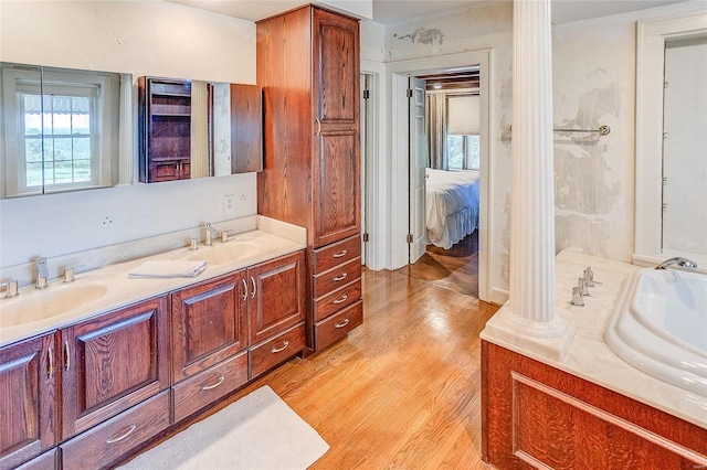 ensuite bathroom featuring wood finished floors, a bath, and double vanity