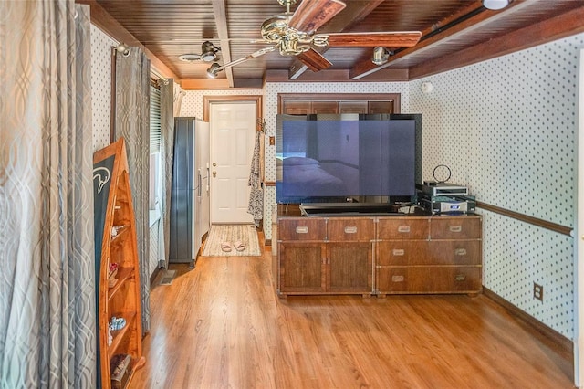 living room featuring wallpapered walls, light wood finished floors, ceiling fan, beamed ceiling, and baseboards