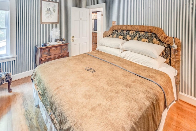 bedroom featuring wood finished floors, wallpapered walls, and baseboards