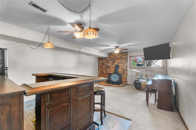 bar area with a wood stove, light carpet, a ceiling fan, and a textured ceiling