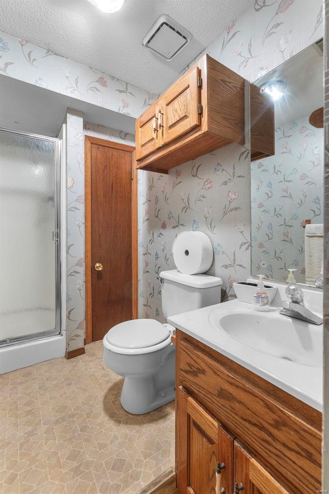 full bathroom featuring wallpapered walls, a textured ceiling, toilet, a shower stall, and vanity