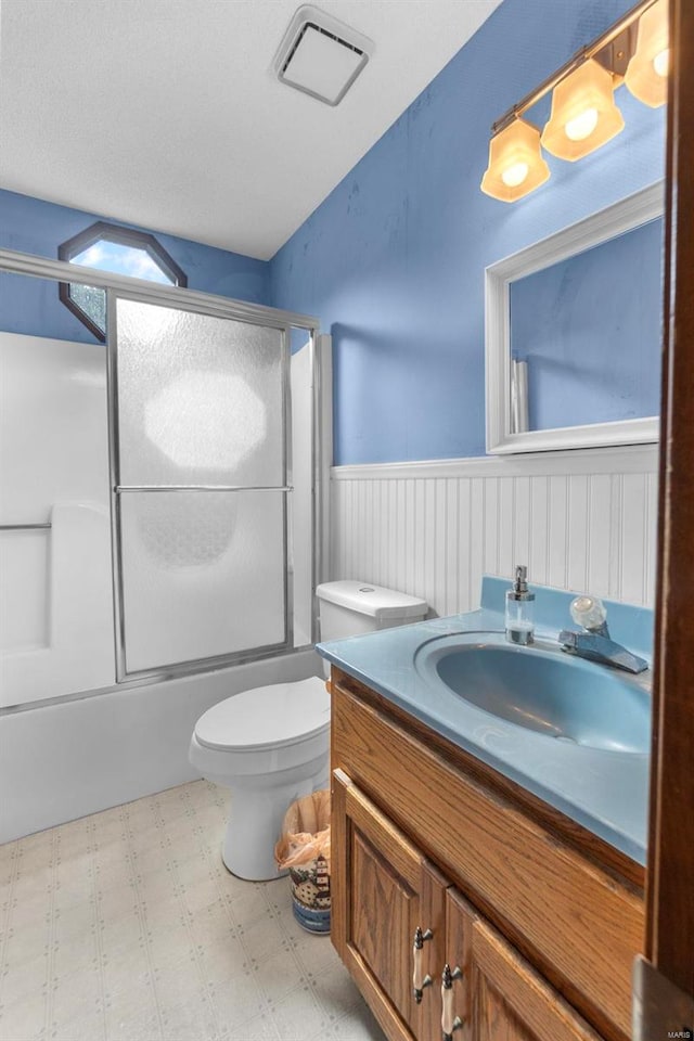 bathroom with wainscoting, tile patterned floors, toilet, vanity, and combined bath / shower with glass door