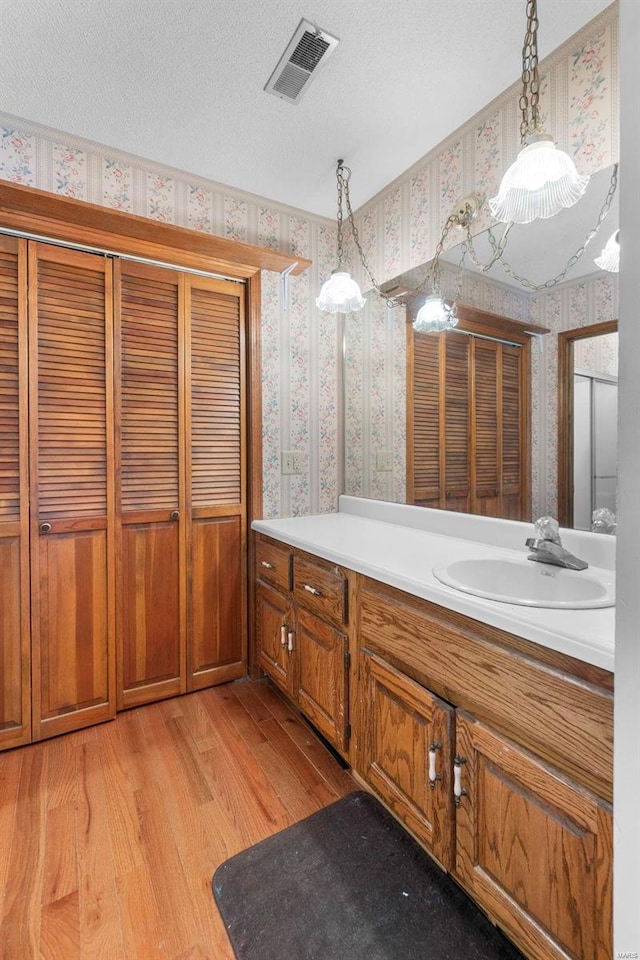 bathroom with wallpapered walls, wood finished floors, a textured ceiling, vanity, and a closet