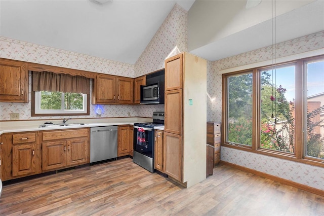 kitchen with stainless steel appliances, wallpapered walls, a sink, light wood-style flooring, and brown cabinetry