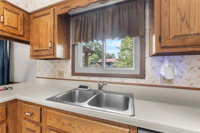 kitchen with wallpapered walls, brown cabinets, a sink, and light countertops