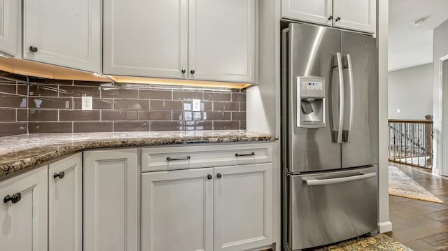 kitchen with stainless steel refrigerator with ice dispenser, backsplash, white cabinets, light stone countertops, and wood finished floors