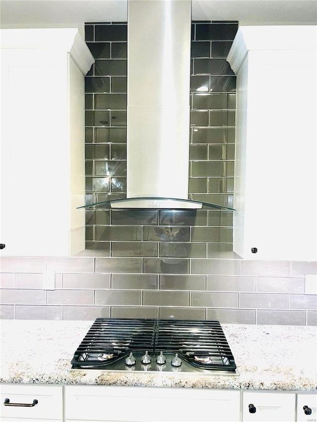 kitchen view of wall chimney exhaust hood, stainless steel gas stovetop, white cabinetry, and light stone countertops