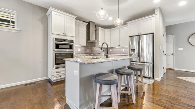 kitchen featuring appliances with stainless steel finishes, wall chimney exhaust hood, baseboards, decorative backsplash, and white cabinets