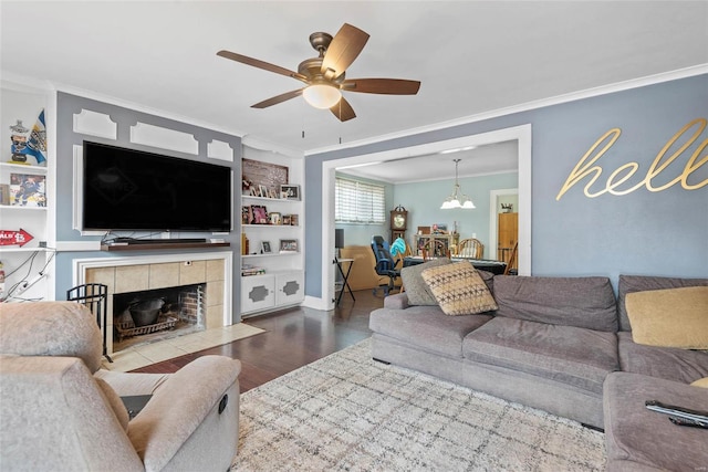 living room featuring crown molding, wood finished floors, a ceiling fan, a tiled fireplace, and built in features