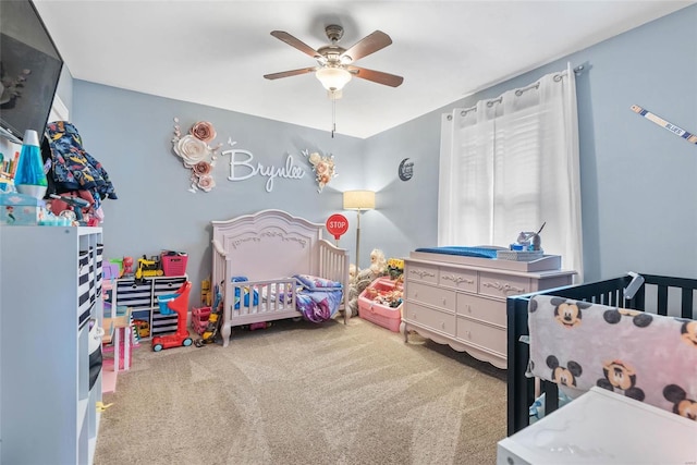 carpeted bedroom featuring a nursery area and a ceiling fan