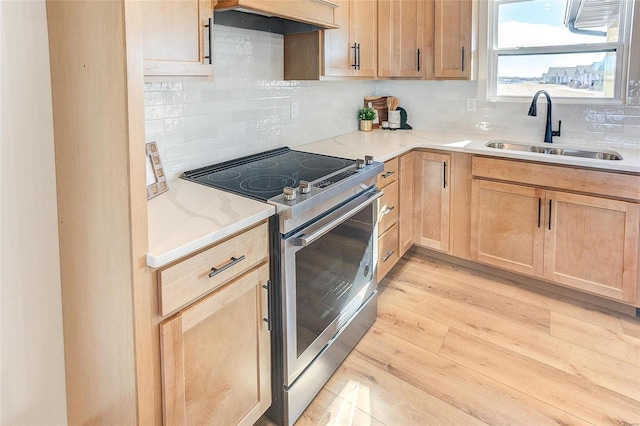 kitchen with stainless steel range with electric stovetop, a sink, light brown cabinets, premium range hood, and tasteful backsplash