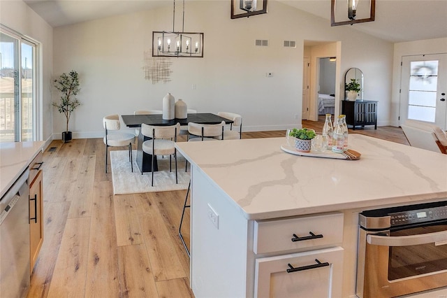 kitchen with lofted ceiling, stainless steel appliances, light wood-style flooring, a kitchen island, and light stone countertops