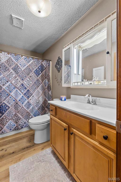 full bath with wood finished floors, toilet, a textured ceiling, vanity, and curtained shower