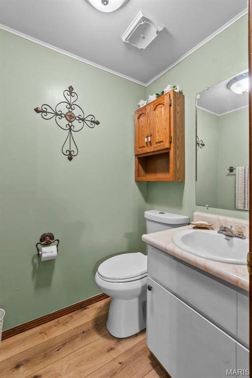 half bath featuring crown molding, wood finished floors, toilet, vanity, and baseboards