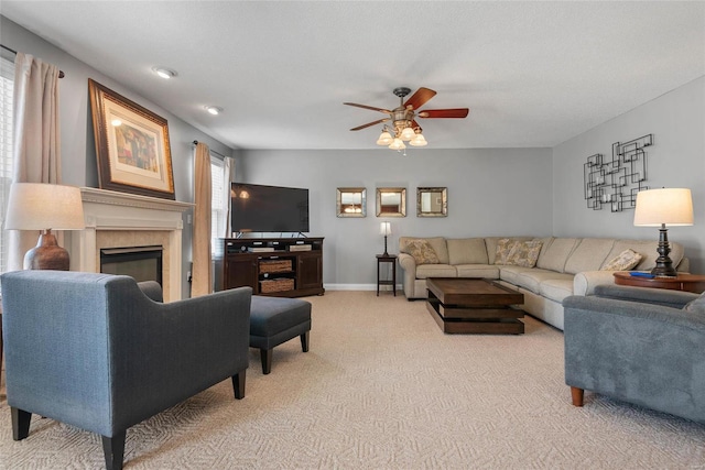 living room featuring ceiling fan, light carpet, a glass covered fireplace, and baseboards