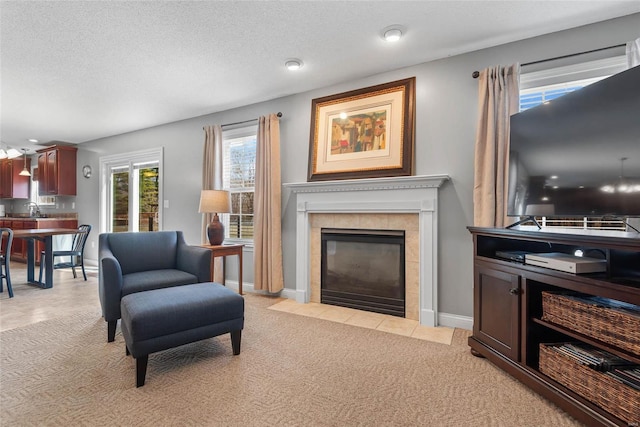 sitting room featuring a tiled fireplace, light colored carpet, and a textured ceiling