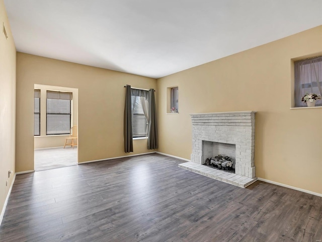 unfurnished living room featuring dark wood-style floors, a brick fireplace, and baseboards