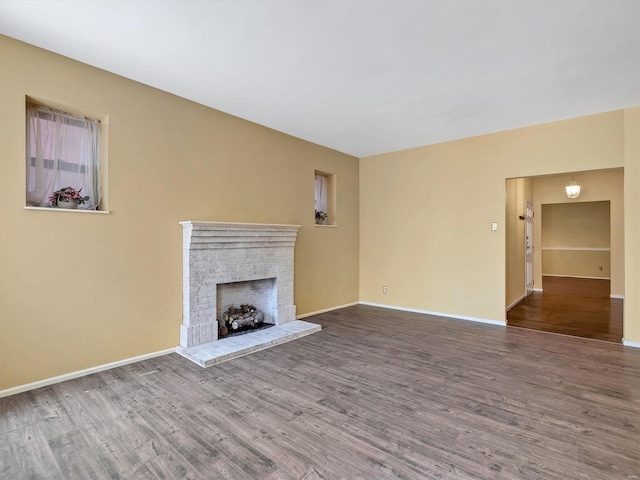 unfurnished living room with wood finished floors, a brick fireplace, and baseboards