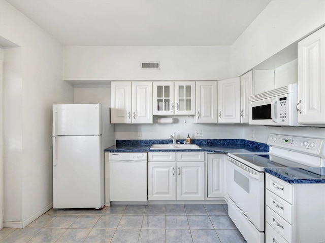 kitchen with white appliances, a sink, white cabinetry, dark countertops, and light tile patterned floors