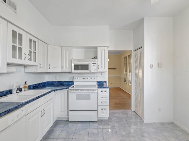 kitchen featuring white appliances, a sink, white cabinets, light tile patterned floors, and glass insert cabinets