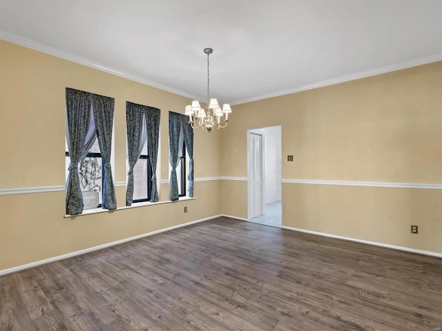empty room featuring a chandelier, wood finished floors, crown molding, and baseboards