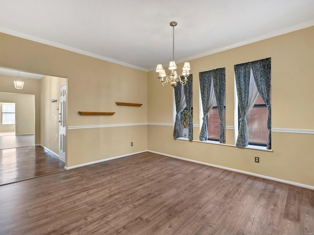 spare room featuring a chandelier, wood finished floors, crown molding, and baseboards