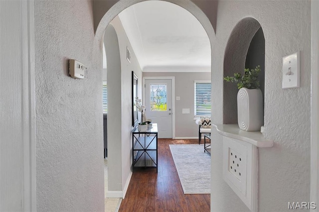 hall with a textured wall, wood finished floors, arched walkways, and baseboards