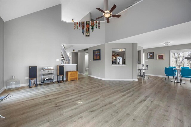 living room with high vaulted ceiling, a ceiling fan, wood finished floors, baseboards, and stairway