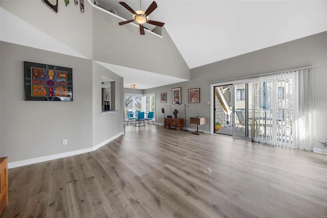 unfurnished living room with ceiling fan, high vaulted ceiling, wood finished floors, and baseboards