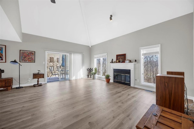unfurnished living room with high vaulted ceiling, wood finished floors, a glass covered fireplace, and baseboards