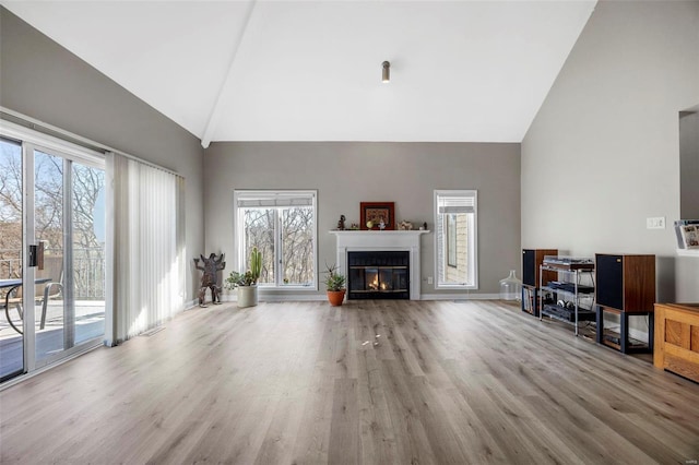 living room featuring high vaulted ceiling, wood finished floors, a glass covered fireplace, healthy amount of natural light, and baseboards