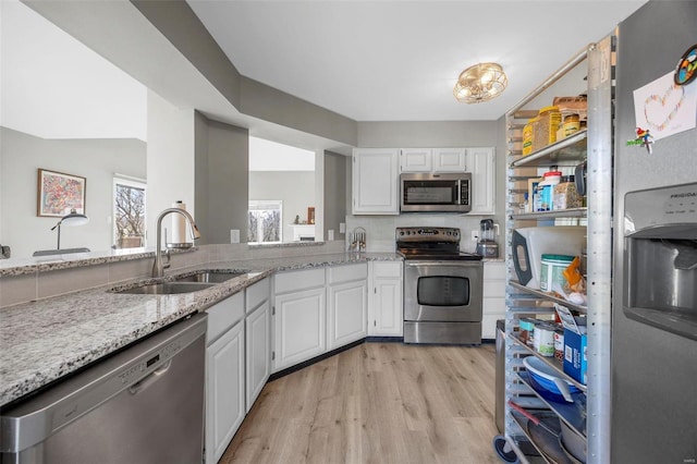 kitchen featuring appliances with stainless steel finishes, a sink, light wood-style floors, and light stone countertops
