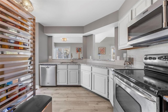 kitchen featuring appliances with stainless steel finishes, a sink, light wood finished floors, and white cabinetry