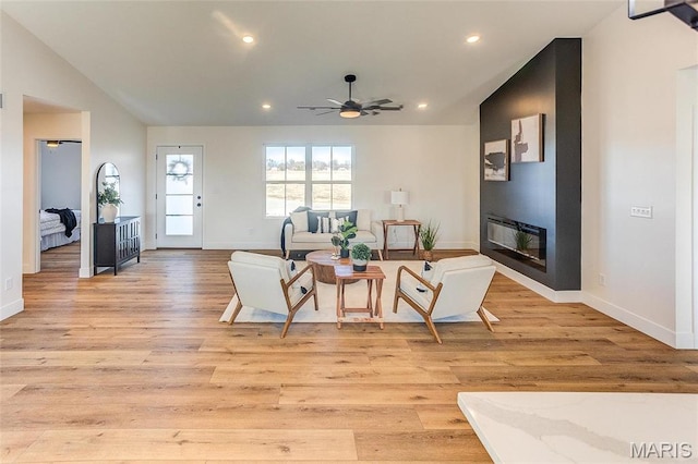 living room featuring light wood-type flooring, a ceiling fan, a glass covered fireplace, recessed lighting, and baseboards