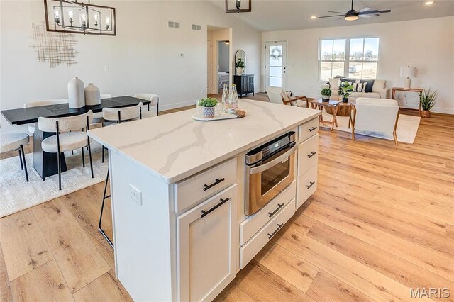kitchen featuring light wood-style floors, white cabinets, a center island, a ceiling fan, and open floor plan